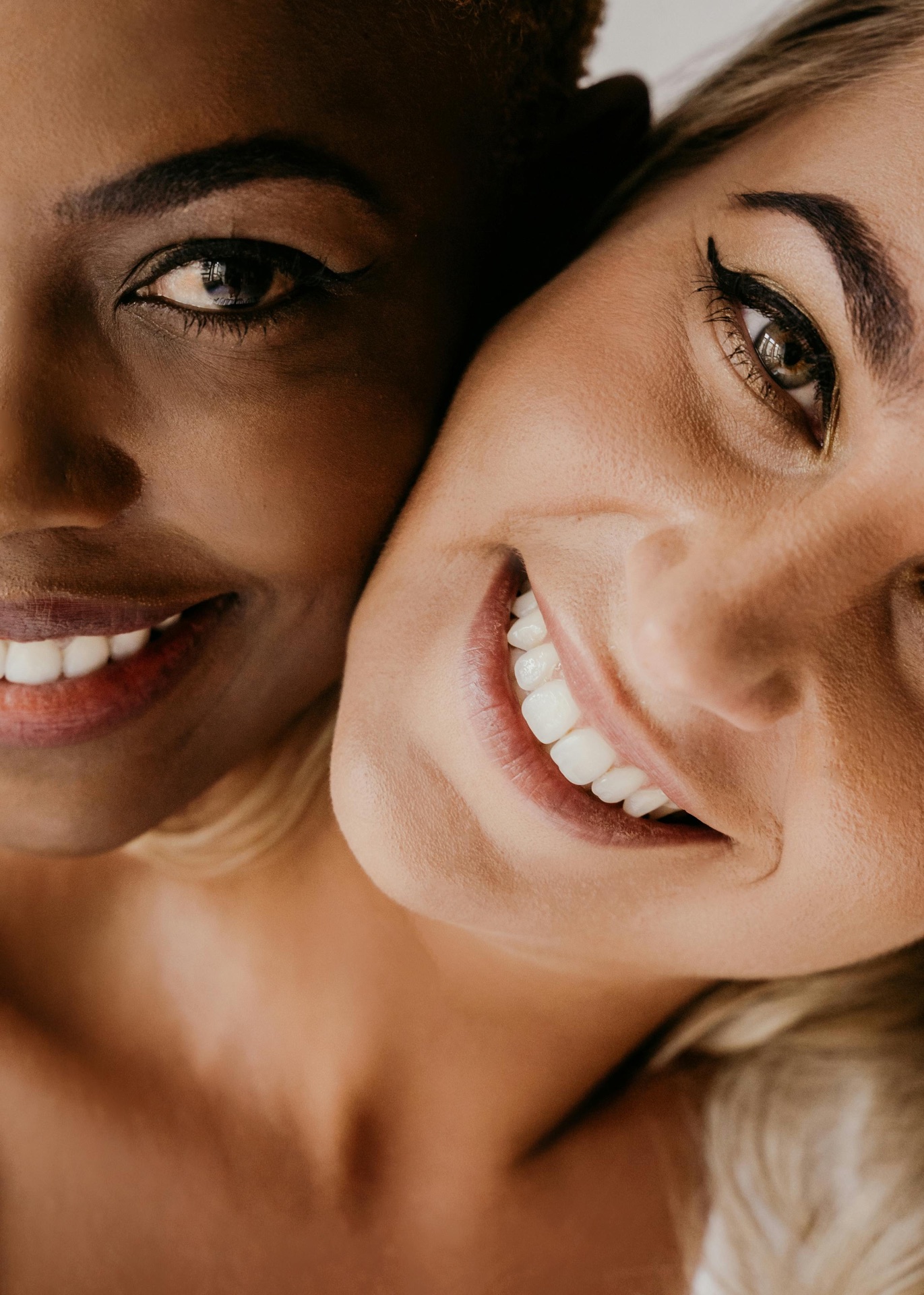 Two women smiling closely together, showing healthy gums and bright teeth